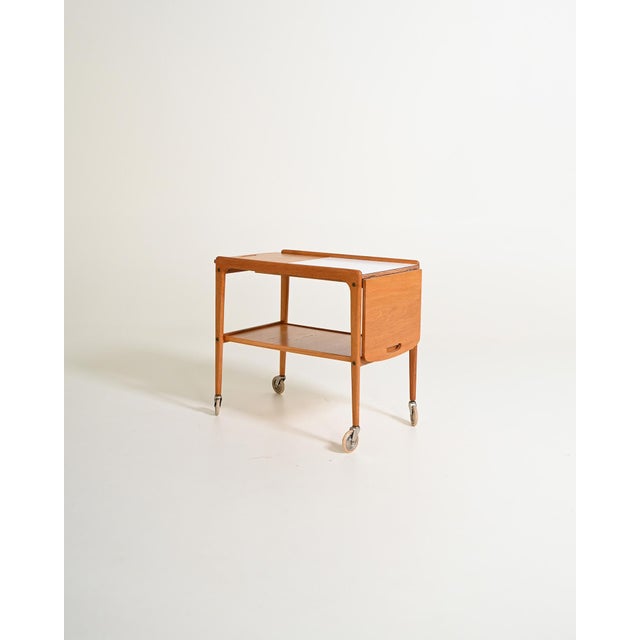 Oak serving trolley with extendable top, white laminate center shelf, and lower shelf. Made in Sweden, 1950s. Introduced...