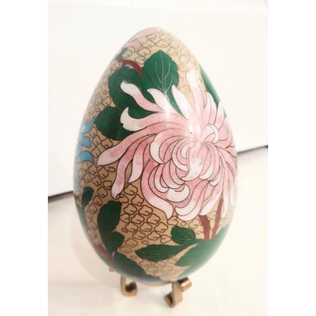 A beautiful floral large Cloisonne egg on a brass stand. The egg features beautiful colors with a large pink, green, red...