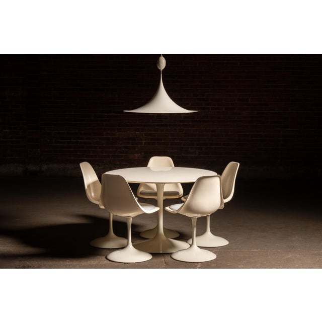 Five-piece tulip-style dining set accompanied by a matching hardwired, sculptural pendant light, all rendered in a...