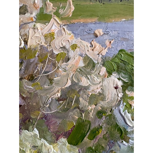 A signed oil painting dated 1977 of Flowering Fruit Trees by the River. A scenic river landscape with blooming fruit trees...