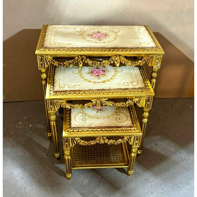 Elegant set of three French-style nesting tables featuring sophisticated gold frames accented with luxurious gold leaf...