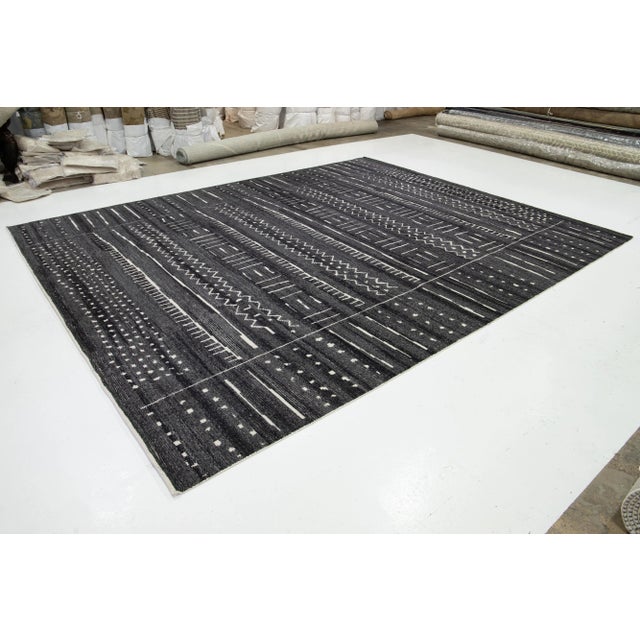 This hand-knotted wool rug in contemporary Moroccan style features a rich charcoal gray and ivory field adorned with an...