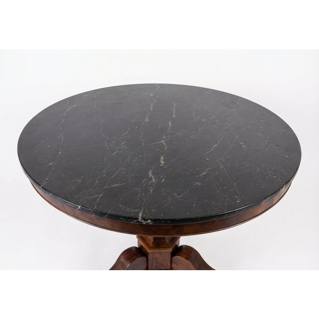 A refined and architecturally balanced French Restauration center table, circa 1825, featuring a honed black marble top...