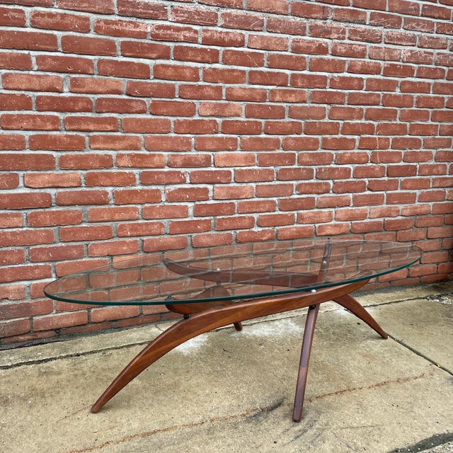 A striking coffee table designed by Forest Wilson, featuring his signature sculptural walnut base beneath a large oval...