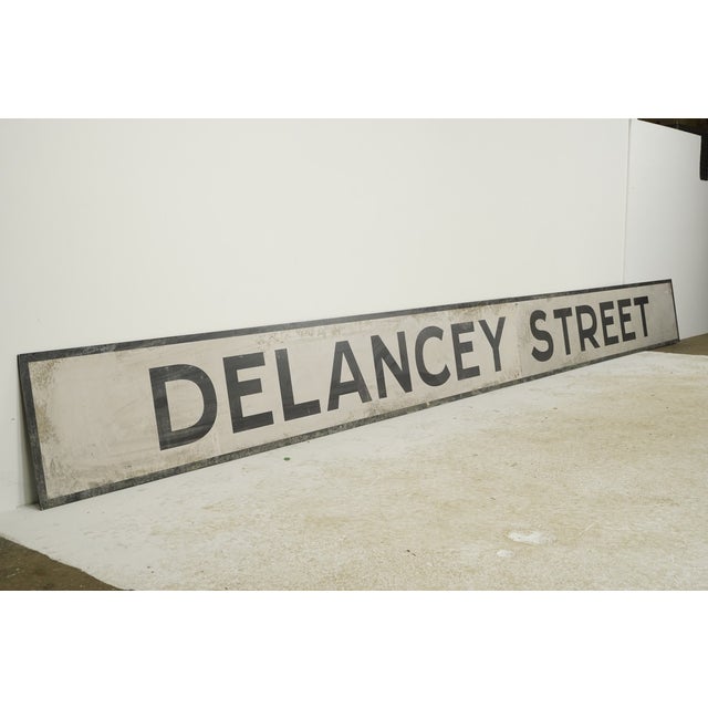 Reclaimed movie set street sign made of plastic foam board in white and black colors. The sign reads "Delancey Street"....