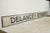 Reclaimed movie set street sign made of plastic foam board in white and black colors. The sign reads "Delancey Street"....