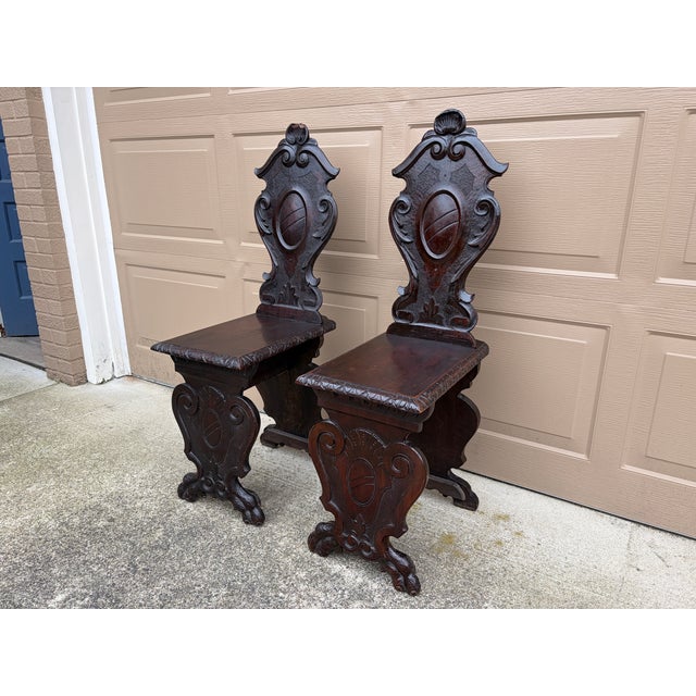 A stunning pair of antique Italian Renaissance walnut hall chairs featuring hand carved shields, stylized shells, and...