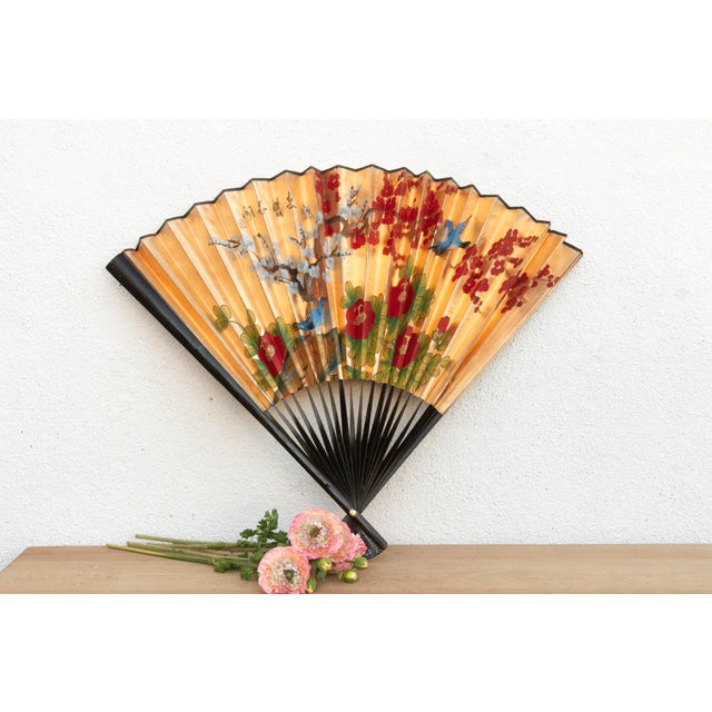A dramatic folding fan featuring a classic Chinoiserie design hand-painted on a shimmering gold background. The artwork...