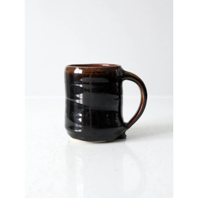 Vintage studio pottery mug, signed by the artist, featuring a rich glossy dark brown glaze with warm, earthy undertones....
