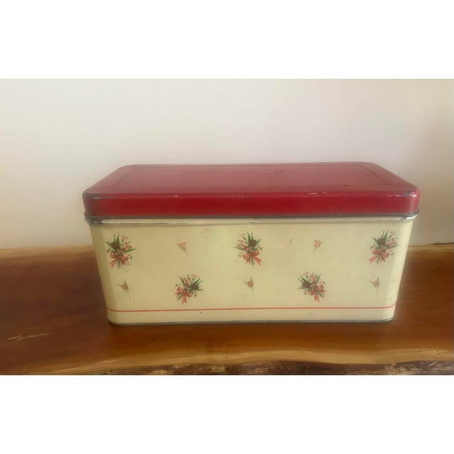 A beautifully sized vintage bread box featuring a soft cream base adorned with scattered floral accents and a bold red...
