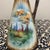 This elegant porcelain pitcher, or ewer, showcases a finely detailed, hand-painted pastoral landscape featuring a woman in...