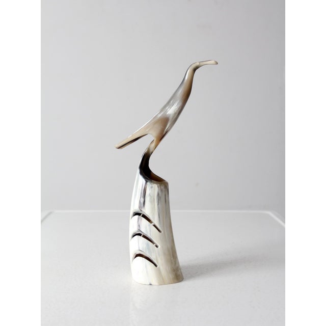 This vintage sculpture features a polished horn bird with a sleek, elongated form perched on a segmented base. The bird's...
