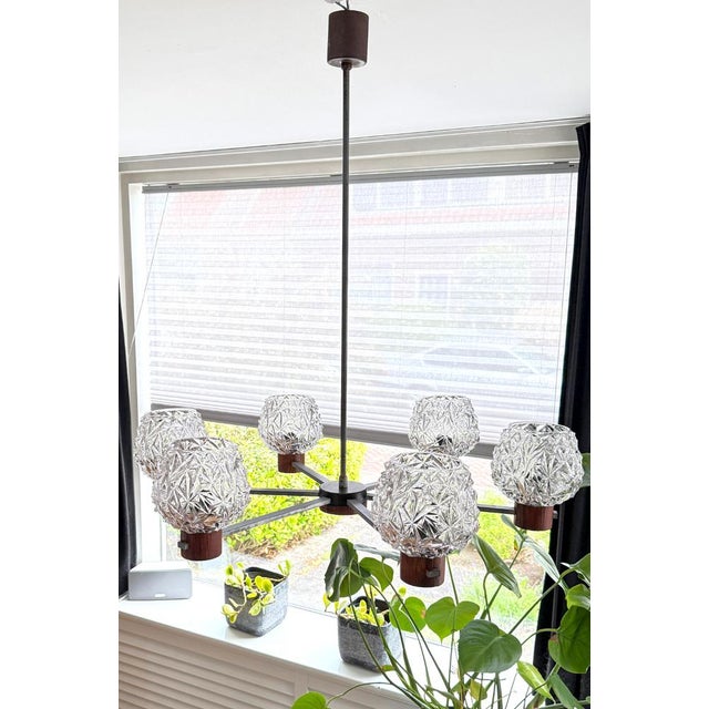This six-arm chandelier combines textured pressed glass shades with warm wood-veneered fittings and a restrained metal...
