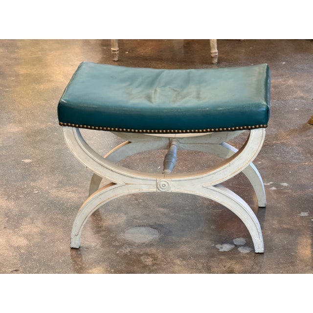 A well-proportioned curule stool on a painted X-frame base with a turned stretcher and carved rosette medallions at the...