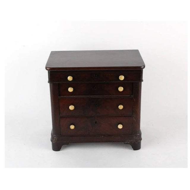 A miniature salesman sample mahogany chest of drawers in a simple, restrained American Empire style in a deep reddish-...