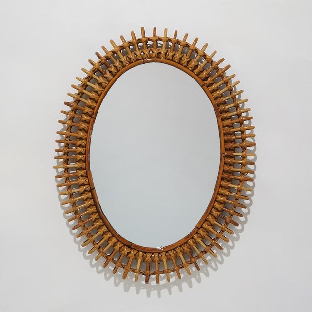 A wall mirror from the 1950s characterised by an oval rattan frame worked into a dense woven pattern. The design develops...