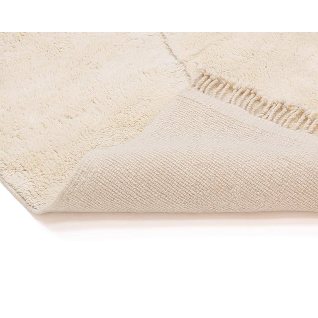 Elegant hand-knotted wool rug in a soft Ivory color, featuring a subtle asymmetric cross pattern that adds a touch of...