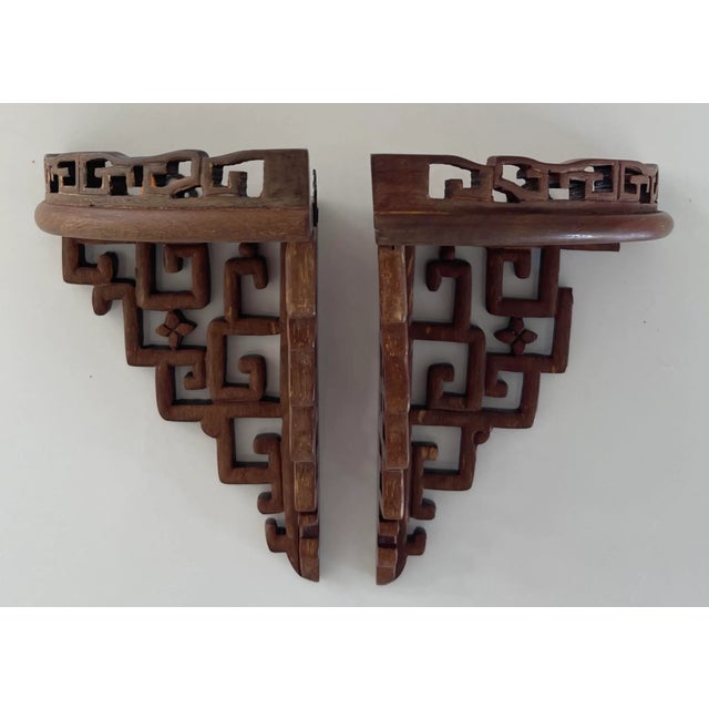 Carved Chinoiserie fretwork corner wall shelves. Brass hanging apparatus attached.