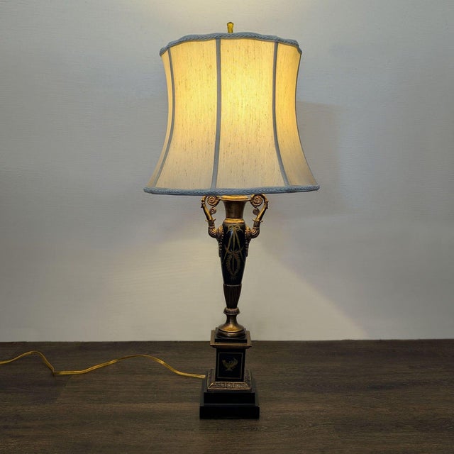 Chelsea House French Neoclassical-style table lamp featuring a black and antiqued gold finish, twin scroll handles, laurel...