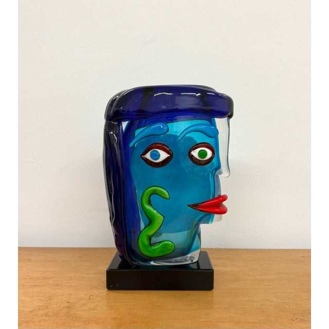 A whimsical sculptural art glass face composed in vivid shades of turquoise, cobalt blue, green, red, white, and brown....