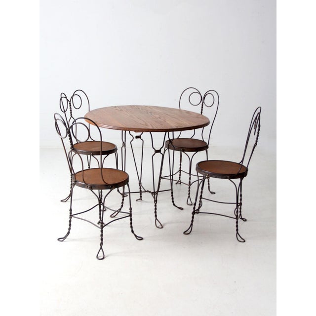 This early 20th-century bistro set features a round iron-base table paired with four matching twisted-wire chairs, each...
