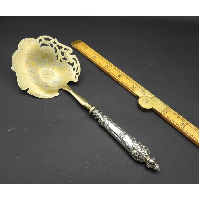 This marvelous antique serving spoon is created with a gorgeous brass bowl that is engraved in a floral motif and pierced...
