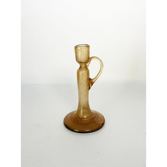 An elegant amber blown-glass candleholder, featuring fine bubbles suspended within the material. Its slender silhouette,...