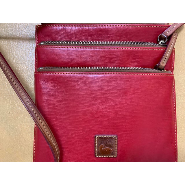 Elegant vintage Dooney & Bourke crossbody bag crafted in rich red leather. The compact design features three individual...