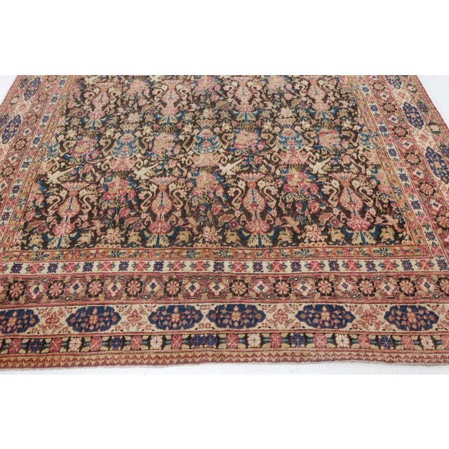 An early 20th century Persian Kerman carpet, the dark brown field with neat rows with alternating floral bouquets, vases...