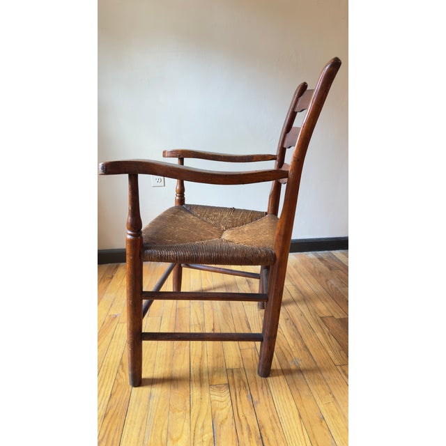 Antique ladder back armchair with a solid wood frame and woven rush seat, dating to the 19th or early 20th century. The...