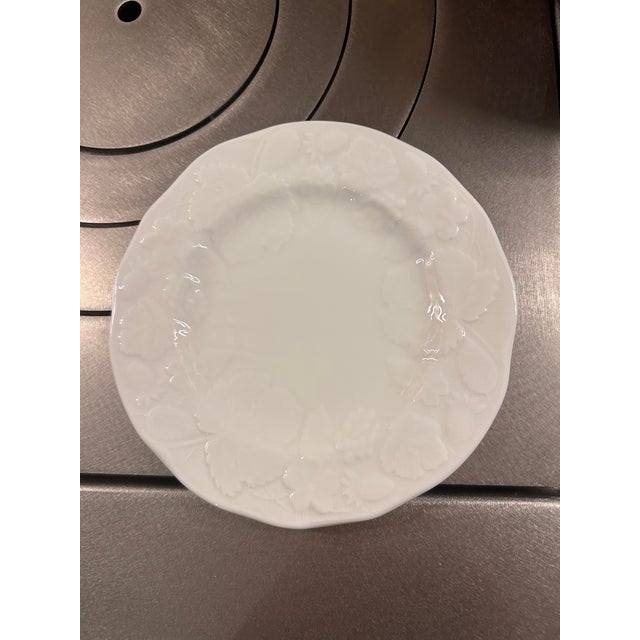 Elegant white bone china bread and butter plates featuring a delicate raised pattern of strawberries, leaves, and trailing...
