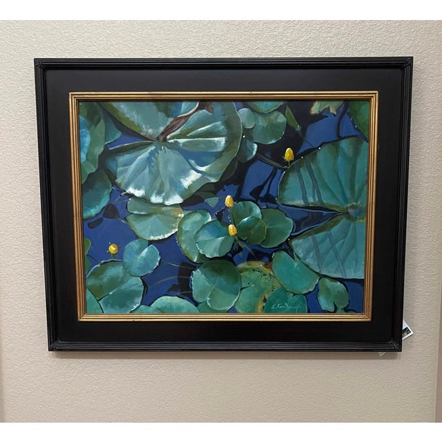 This artwork presents a serene view of a pond, where vibrant green lily pads float gracefully atop deep blue water. The...