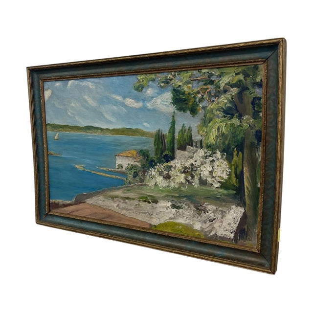 Vintage coastal landscape painting depicting a shoreline scene with a sailboat on calm blue water, a white stucco-style...