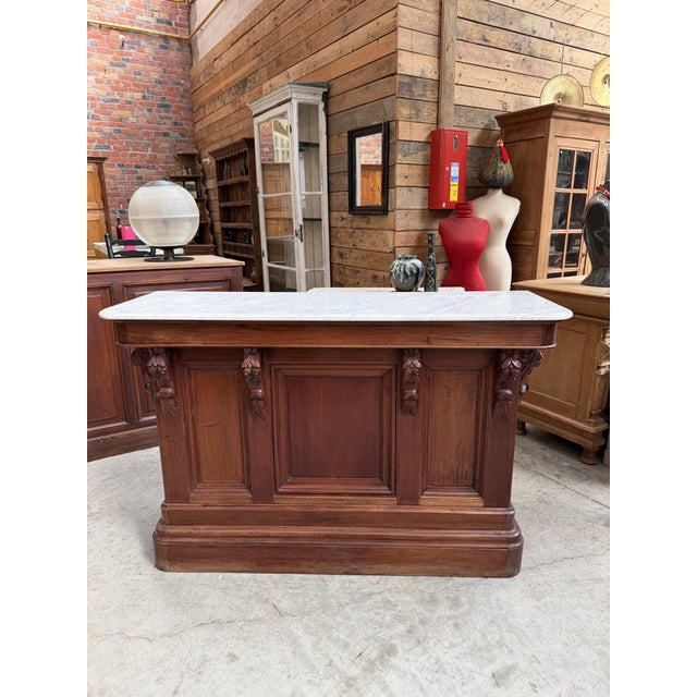 This antique bar counter has been fully restored. It features a marble top and a mahogany base with carved scrollwork. On...