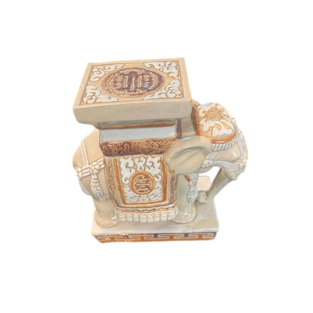 A sculptural ceramic elephant rendered in a warm neutral glaze, designed as a decorative plant stand or tabletop pedestal....