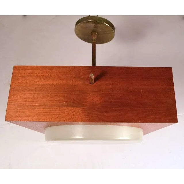 Square wood box form body, with off-white circular glass insert, supported by solid brass rod arms. Fixture features three...