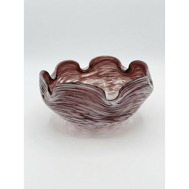 A charming vintage handblown glass bowl in the style of Murano, featuring a ruffled organic form and swirling plum and...