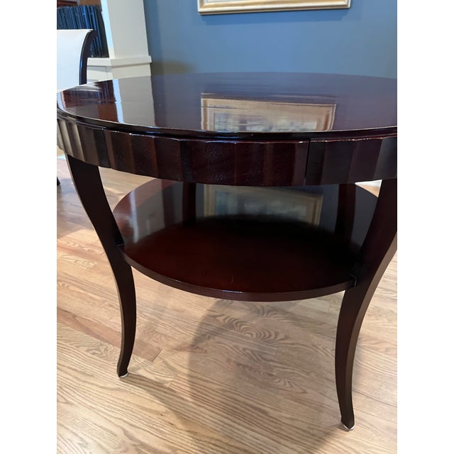 This polished wood side table has a dark mahogany finish and a round silhouette. This piece has a single integrated drawer...