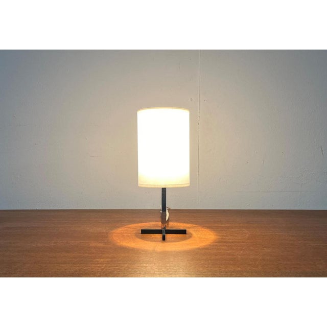 Little mid century table lamp with a special foot. A minimalist design. The simple foot of black painted square bars is...