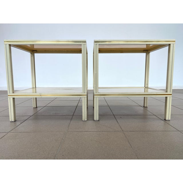Dimensions: H 20.3” x W 19.5” x D 16” Pair of Pierre Vandel Paris cream aluminum two-tier side tables with glass shelves....