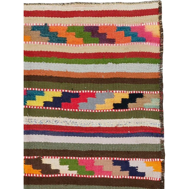 This mid-20th century Persian flatweave kilim rug presents a lively horizontal composition defined by rhythmic striping...