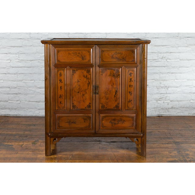 An antique Chinese natural wood finish cabinet from the early 20th century with hand-painted black calligraphy, figures...