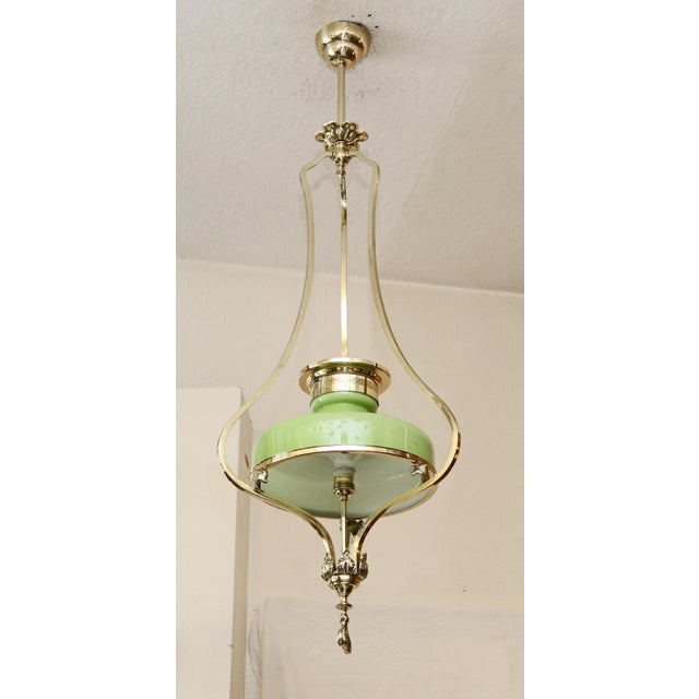 Art Nouveau chandelier, circa 1900. Curved, square brass profiles with floral motifs. Light green overlay glass shade. The...