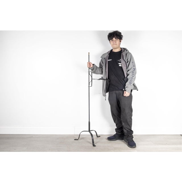 An18th century wrought iron floor lamp or standing candelabra with a slender vertical shaft, adjustable swivel arm...