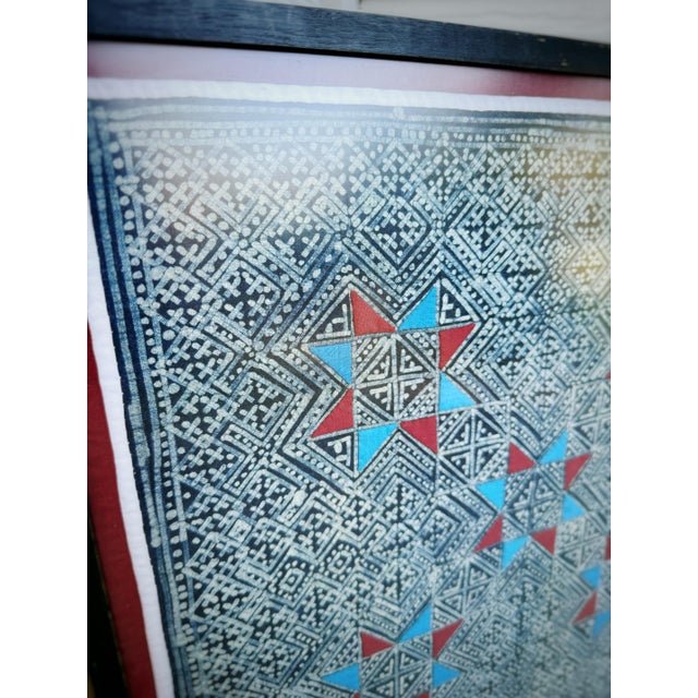 A striking vintage framed textile artwork featuring an intricate indigo geometric pattern accented with vibrant red and...
