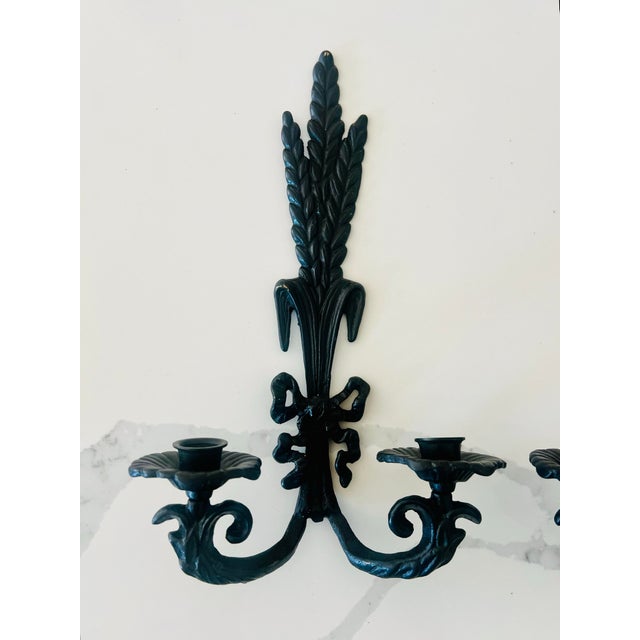This pair of vintage wrought iron sconces are designed to hold taper candles and showcase a decorative wheat or leaf motif...