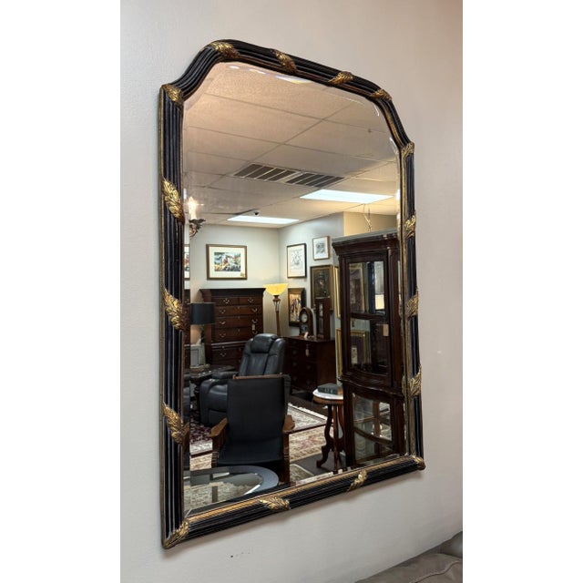 This La Barge Regency-style wall mirror pairs a deep black frame with elegant gold leaf-style accents, including sculpted...