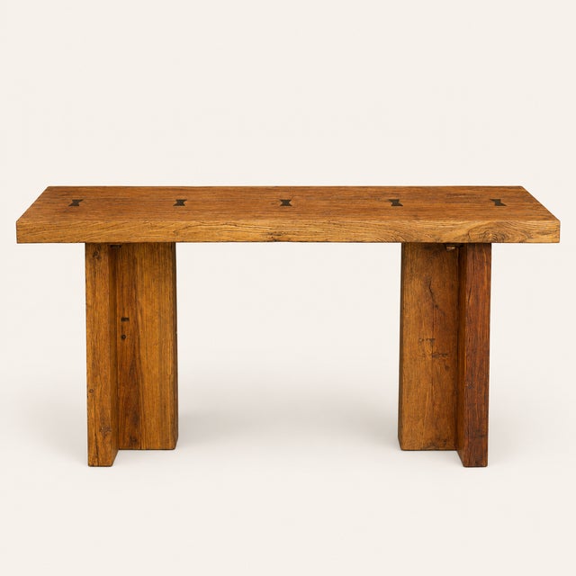 A substantial reclaimed wood console table, likely elm or fir, featuring a thick plank top joined with inset brass...