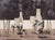 In "Glass Titans," two skulls dominate the composition, surrounded by an array of glass containers and tools, creating a...