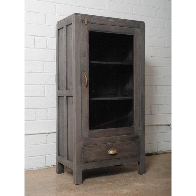 This character-rich wooden glass-front cabinet features a beautifully weathered gray-washed finish that enhances the...